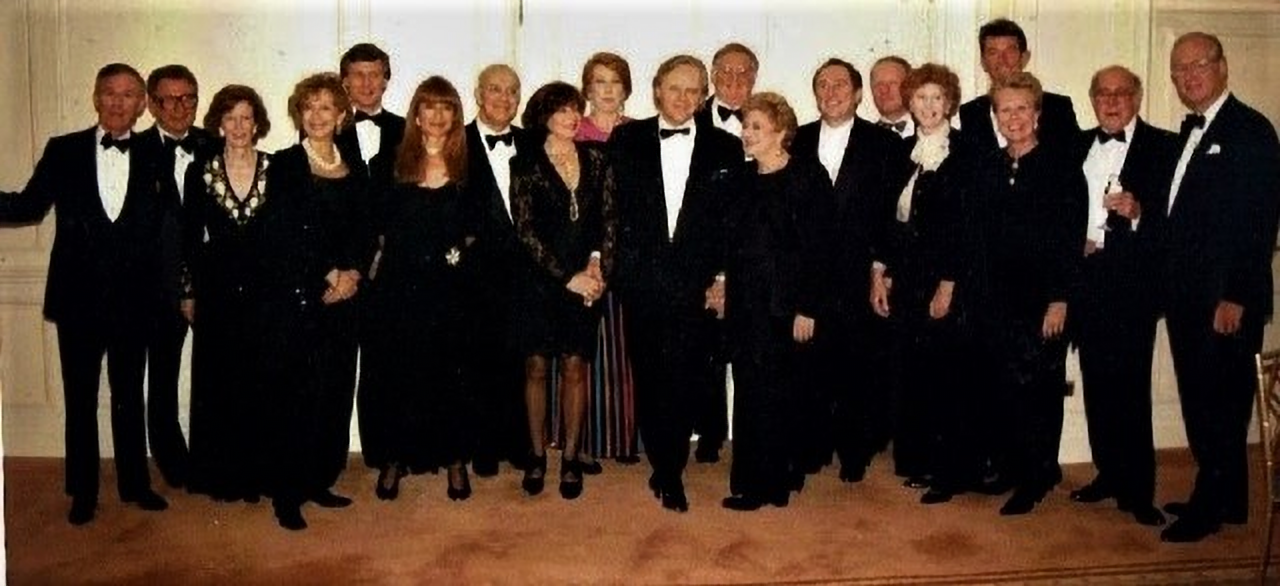 Group photo of Anthony Hopkins standing in the centre of a number of others, smiling for the camera. They are all in black tie evening wear.