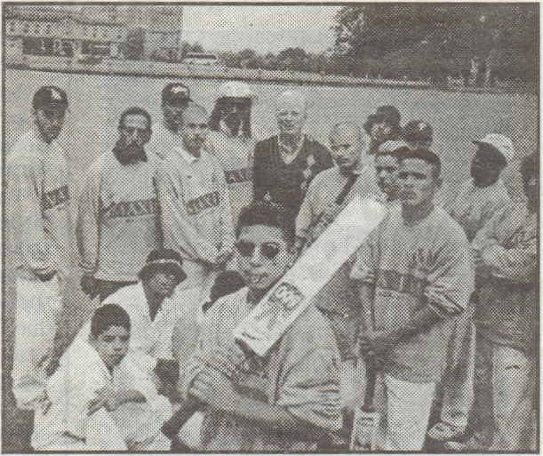 Black and white scanned photo of the team in their uniforms, standing on the pitch at Castle Ashby. In the background is the house.